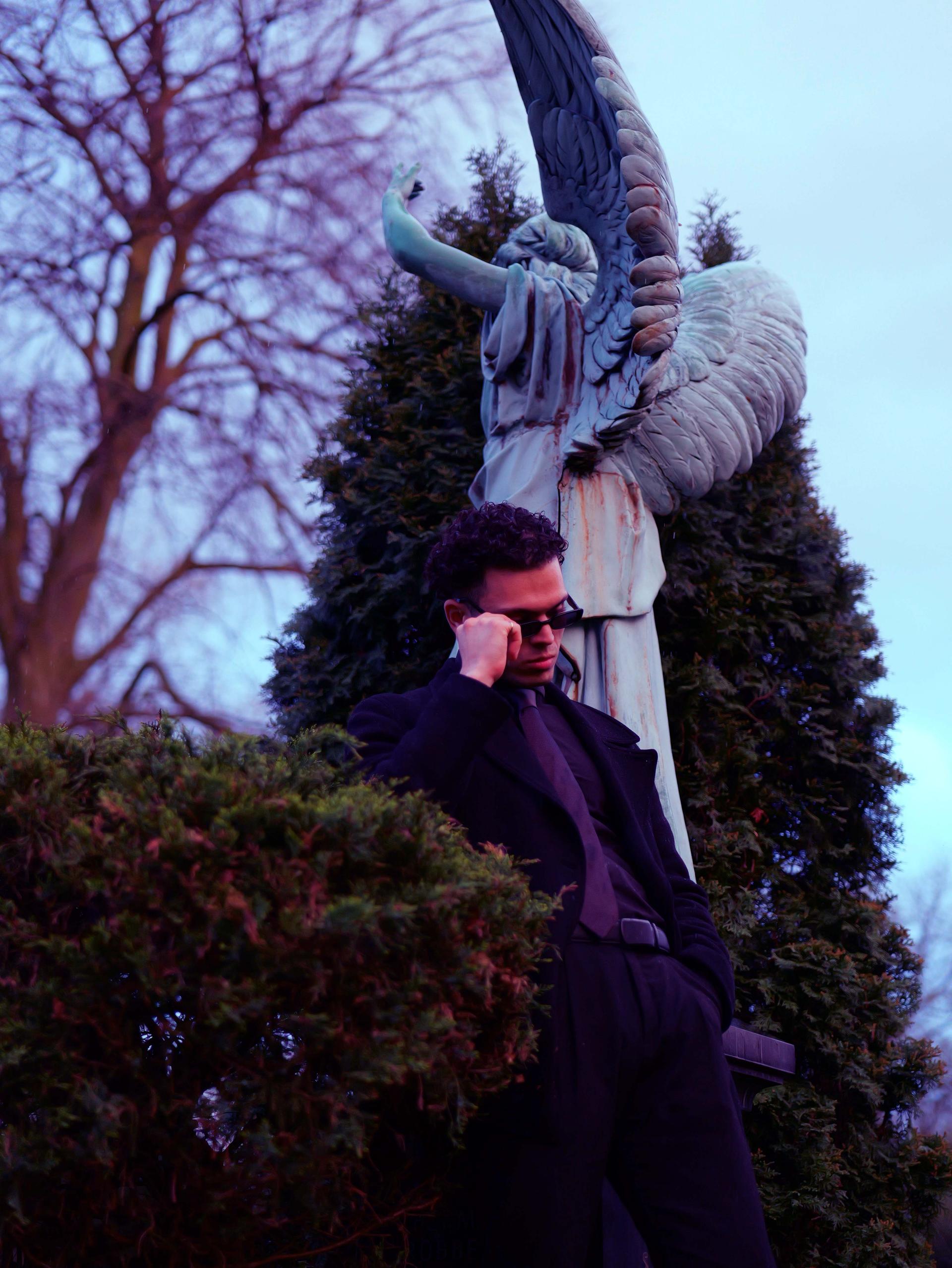 leaning on the guardian angel in a black suit and tie